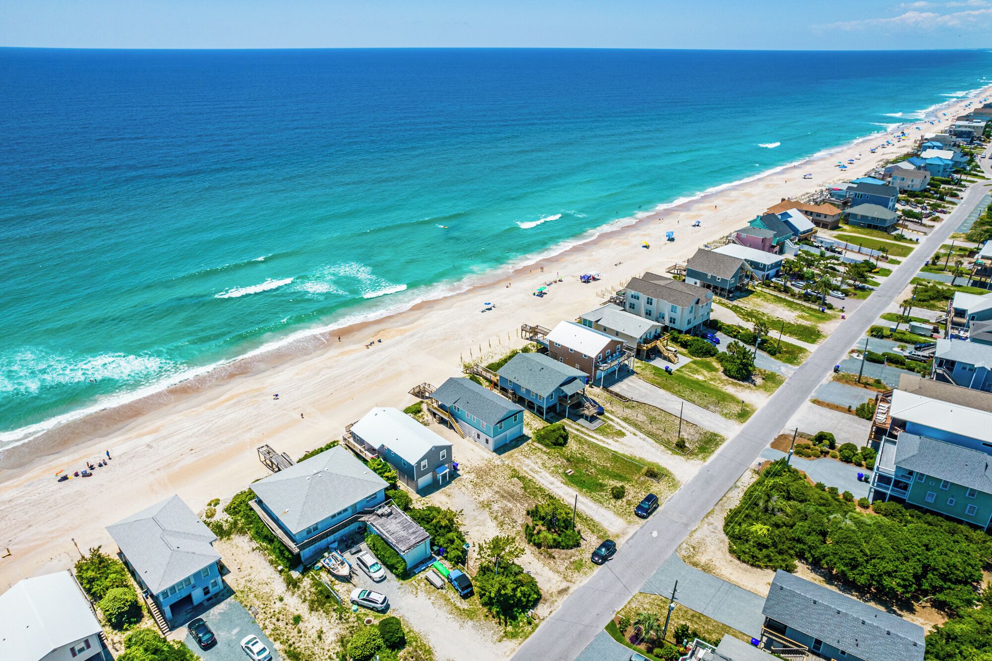Vue aérienne d’une zone résidentielle côtière, avec des maisons, une plage et l’océan.