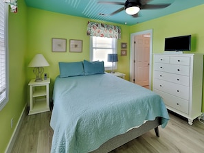 A bedroom with a bed, a nightstand, a dresser, a ceiling fan, and a window with blinds. - Lungomare by Topsail Realty (Holly Ridge)