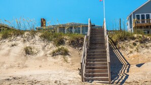 A wooden staircase leading to a building with a flag on top, surrounded by sand and sparse vegetation. - S.O.B. (Sweet Ol' Bill) by Topsail Realty (Holly Ridge)