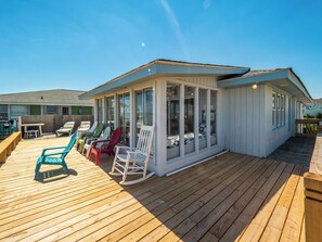 A covered outdoor deck with wooden flooring, a glass enclosure, and several Adirondack chairs. - S.O.B. (Sweet Ol' Bill) by Topsail Realty (Holly Ridge)