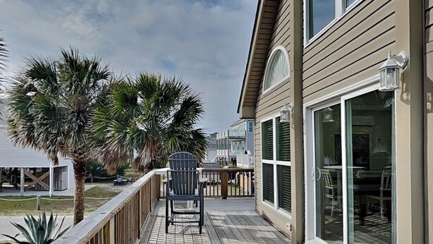 A wooden deck with a chair, palm trees, and a building with large windows.