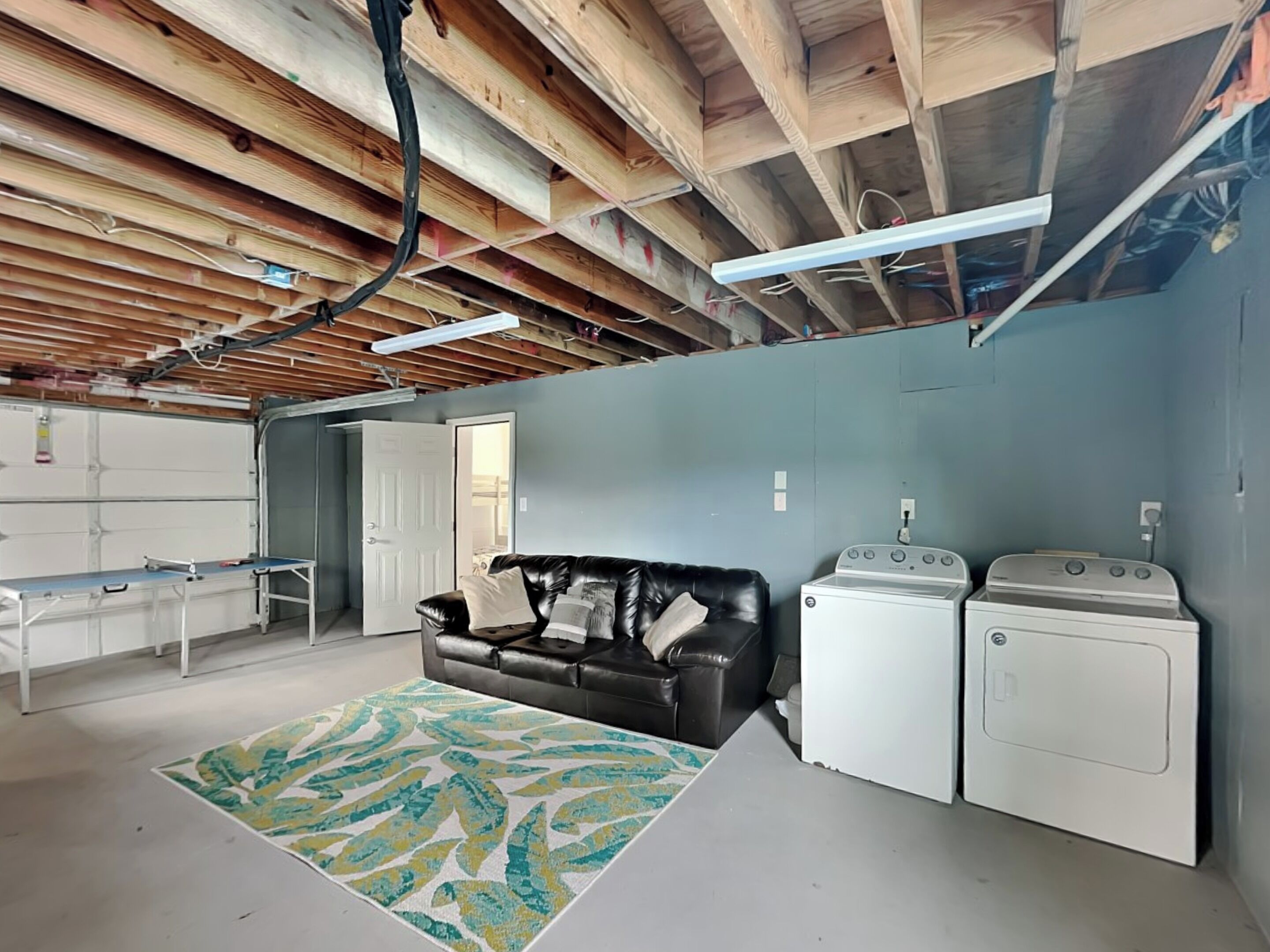 A laundry room with a black leather couch, two washing machines, and a large rug.