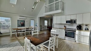 A spacious kitchen with white cabinets, a dining area with a wooden table and white chairs, and a pool table in the background.