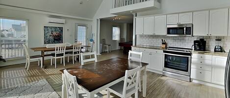 A spacious kitchen with white cabinets, a dining area with a wooden table and white chairs, and a pool table in the background.