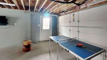 A room with a ping pong table, a wooden barrel, and a door with a window.