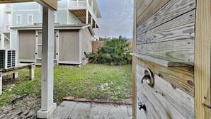 A wooden deck with a view of a backyard, a white fence, and a building in the background.