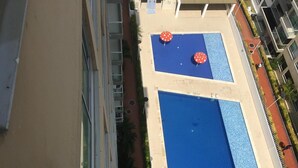 Un espace piscine aménagé sur le toit, comprenant deux piscines, entouré d’un petit muret et bordé d’un chemin.