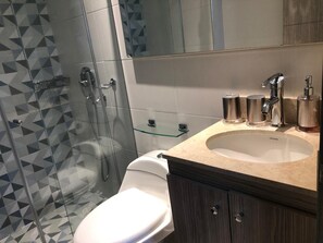Une salle de bain avec une douche à parois de verre, des toilettes blanches, un lavabo avec un plan de toilette beige et un miroir au-dessus du lavabo.