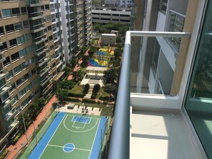 Un immeuble de grande hauteur doté de nombreux balcons donnant sur un terrain de sport et sur la végétation environnante.