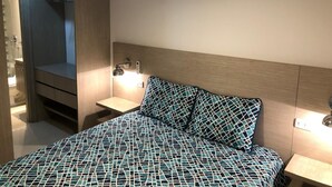 Une chambre à coucher comprenant un lit, des tables de chevet, un téléviseur fixé au mur et un placard intégré.