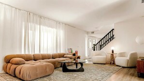A living room with a sectional sofa, a coffee table, and a staircase. - 5BR Fun Haven: Pool, Mini Golf, Movie, Gameroom (Riverside)