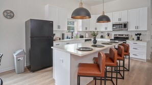 A modern kitchen with white cabinets, a black refrigerator, a central island with bar stools, pendant lighting, and a clock on the wall. - Generous 4BR 3BA Charmer Near Glorius Downtown (San Antonio)