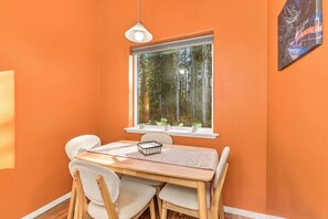 Un coin repas comprenant une table, des chaises, une fenêtre donnant sur les arbres et un luminaire suspendu.