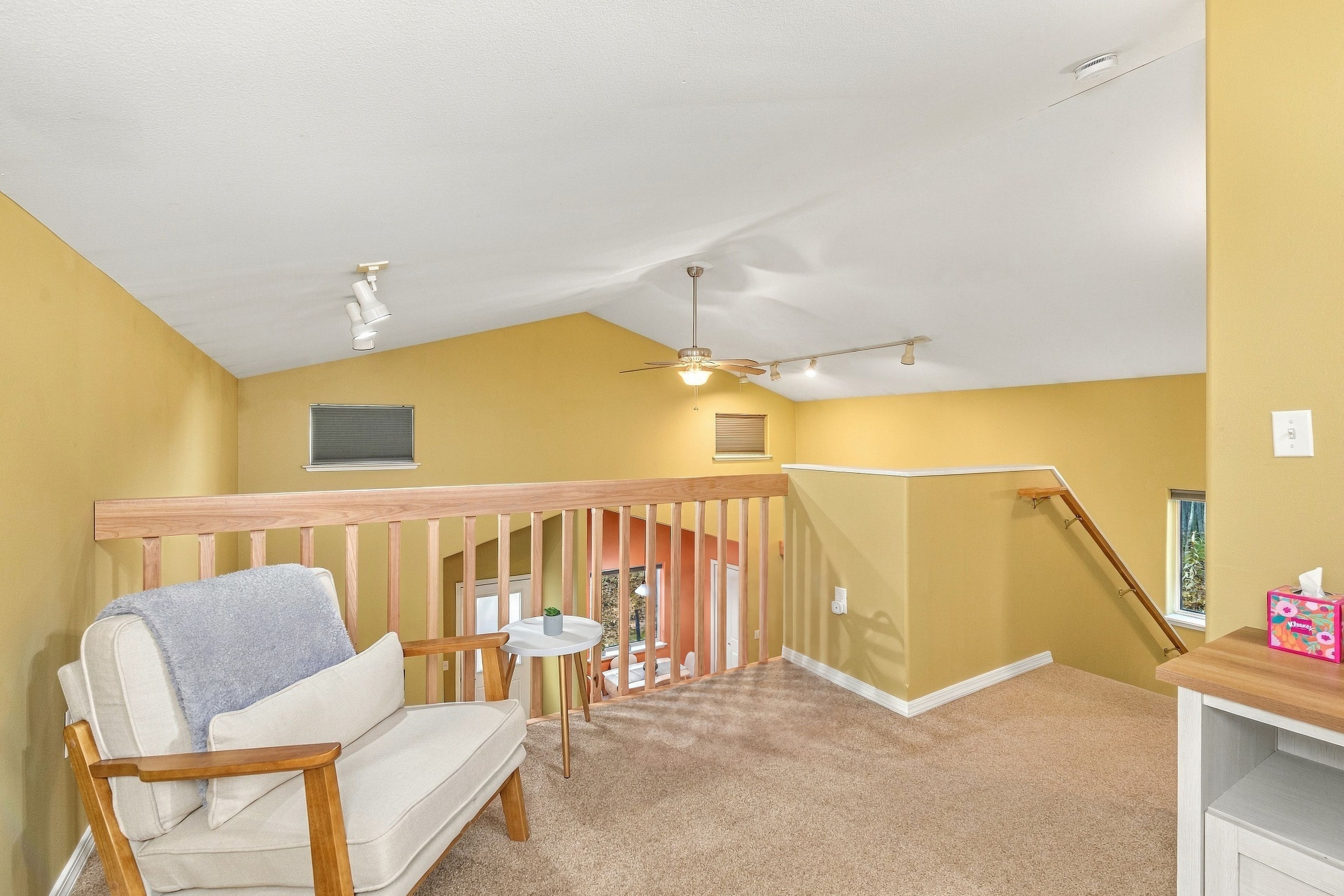 Une pièce avec un plafond en pente, une chaise en bois, une petite table, un ventilateur de plafond et un escalier menant à un autre niveau.
