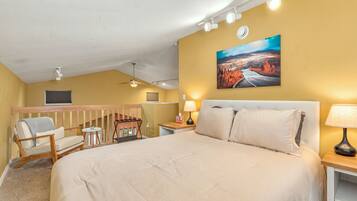 Une chambre d’hôtel avec un grand lit, une chaise, un bureau, un tableau au mur et un ventilateur de plafond.