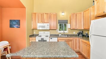 Une cuisine avec des meubles en bois, un réfrigérateur blanc, un four à micro-ondes, une cuisinière et un plan de travail en granit.