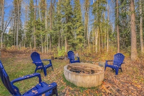 Un décor forestier avec un foyer et quatre chaises bleues disposées autour.