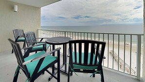 Een balkon met stoelen en een tafel, met uitzicht op een strand met een hek en een trap.