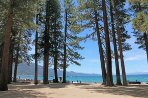 A beach with tall pine trees, a sandy area with benches, and a view of the sea and mountains in the background. - Charming 3-bedroom Ski Cabin on Golf Course in lovely Incline Village (Incline Village)