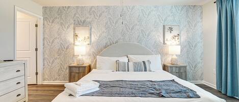 Une chambre à coucher avec un lit, des tables de chevet, un ventilateur de plafond et une porte.