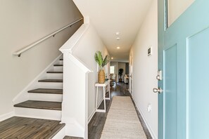 A hallway with a wooden staircase, a white console table with a plant, and a blue door. - 2 Mi to Shore: Newly Built Surfside Beach Gem (Surfside Beach)