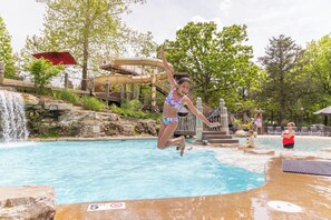 A person jumping into a pool with a water slide and a waterfall in the background.