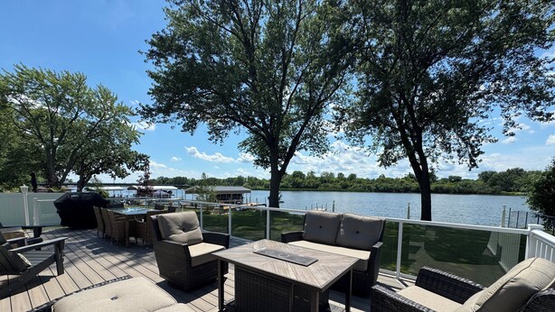 A deck with outdoor furniture, a grill, and a view of a lake. - Riverfront Oasis with Fun + Relaxation for All, McHenry (McHenry)