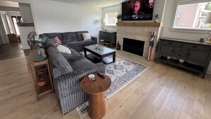 A modern living room with a sectional sofa, a fireplace, a flat-screen TV, and a dining area with a wooden table and chairs. - Riverfront Oasis with Fun + Relaxation for All, McHenry (McHenry)