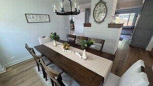 A dining area with a wooden table, white chairs, and a chandelier. - Riverfront Oasis with Fun + Relaxation for All, McHenry (McHenry)