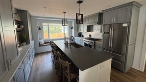 A modern kitchen with grey cabinets, a large island, stainless steel appliances, and a view to the outside. - Riverfront Oasis with Fun + Relaxation for All, McHenry (McHenry)