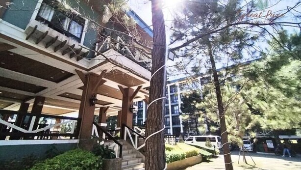 A building with a covered outdoor area, stairs leading to an upper level, and a tree in the foreground.