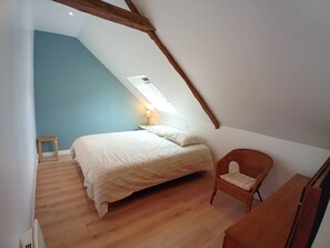 Ein Schlafzimmer mit schrägem Dach, einem Bett, einem Stuhl und einem kleinen Hocker.