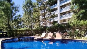Una piscina con sillas de descanso, rodeada de árboles y un edificio de varios pisos con balcones.