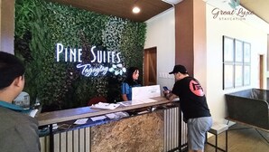 Un mostrador de recepción con el letrero de Pine Suites, un área de recepción con una pared verde y un letrero que dice Great Luxe Staycation.
