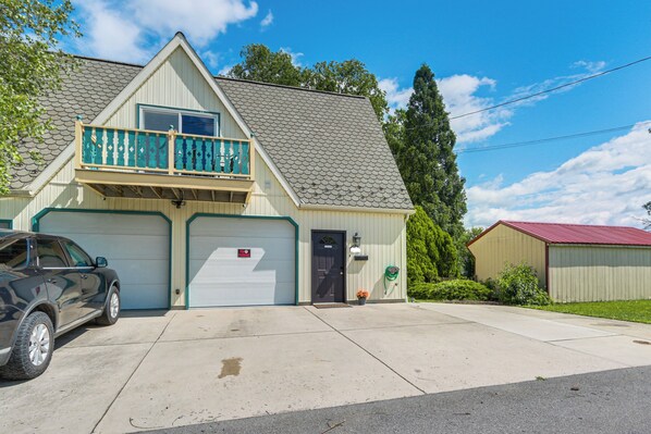 A two-story building with a garage, a balcony, and a red-roofed shed. - Walk to Town: Charming Unit w/ Balcony in Bedford! (Bedford)