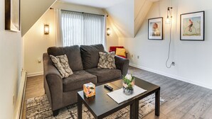 Een woonkamer met een bruine bank, een salontafel, een vloerkleed en twee wandlampen.