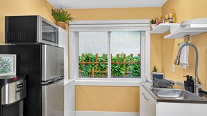 A compact kitchen with a microwave, refrigerator, and sink. There's a window with a view of a wooden fence and greenery. - Private Studio/1 Min-Hospital/Self Check-In/75" TV (Williams Lake)