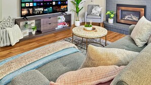 A modern living room with a flat-screen TV, a grey sofa, a round coffee table, and a fireplace. - Cozy Suite/1 Min-Hospital/Full Kitchen/Sleeps 4 (Williams Lake)