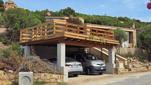 A building with a wooden deck, a car parked under a covered area, and a stone wall. - Villa Stella Oasis of Peace in the Natural Park of Costa Paradiso Sardinia (Costa Paradiso)