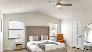 Une chambre avec un grand lit, un ventilateur de plafond, une chaise et un miroir.