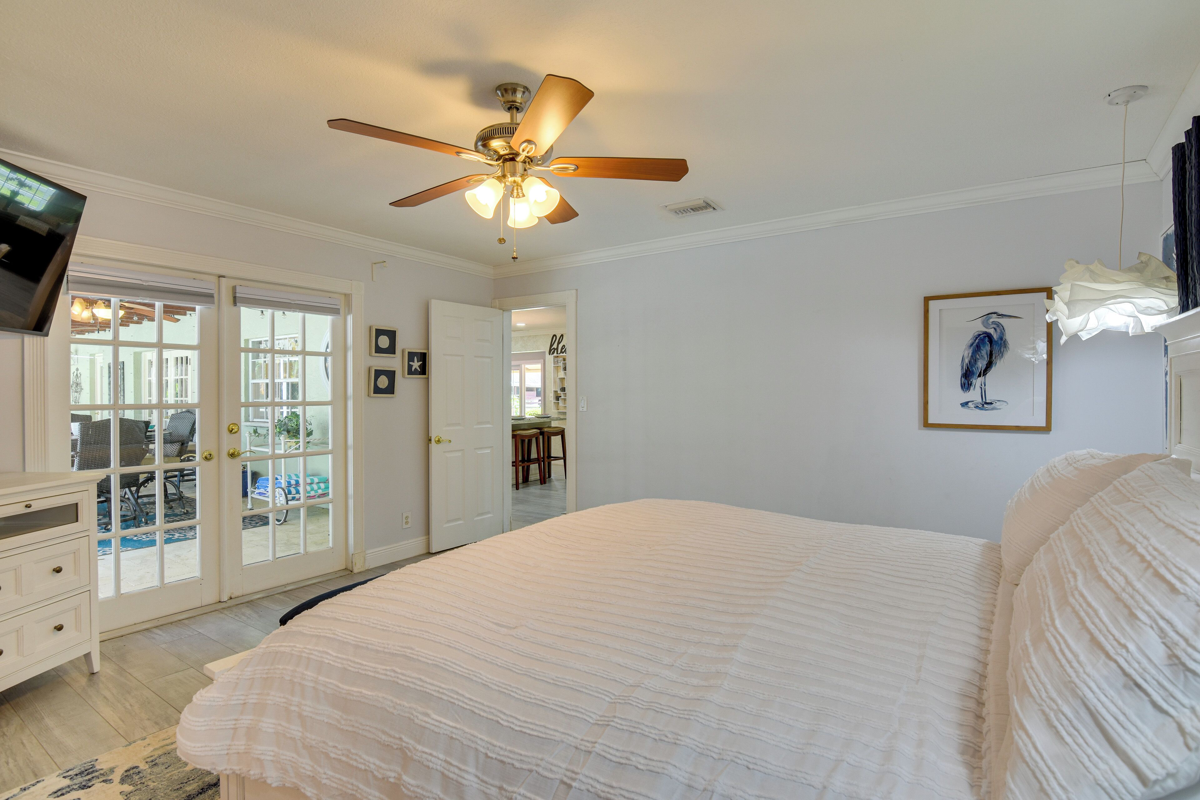 A bedroom with a large bed, a ceiling fan, a TV, and a door leading to a balcony.