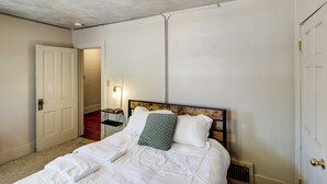 A bedroom with a wooden headboard, white bedding, and a nightstand with a lamp. - 1 Mi to UNL: Group Getaway w/ Game Area (Lincoln)