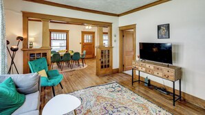 A spacious living room with a wooden floor, teal chairs, a white sofa, a TV on a wooden stand, and a dining area in the background. - 1 Mi to UNL: Group Getaway w/ Game Area (Lincoln)