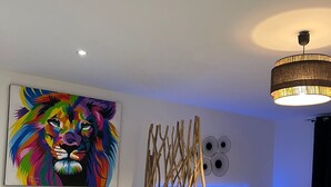 A modern bedroom with a large colorful lion painting, a bed with white linens, a dark blue sofa, and a unique wooden structure. - Ty paradis (Saint-François)