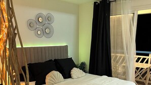 A bedroom with a bed, bedside tables, a decorative wall piece, and a balcony with a chair. - Ty paradis (Saint-François)