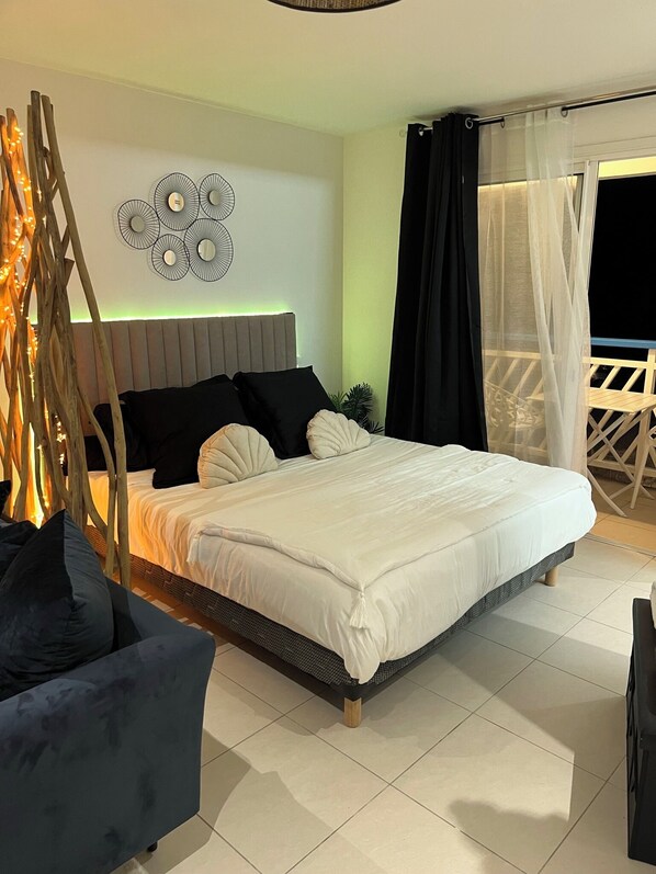 A bedroom with a bed, bedside tables, a decorative wall piece, and a balcony with a chair.