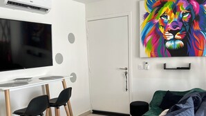 A modern living room with a sofa, a TV, a dining area with chairs, and a colorful painting on the wall. - Ty paradis (Saint-François)