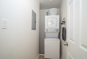 A laundry room with a stacked washer and dryer, a basket on top, and a door with a towel rack. - Historic Comfort 2BR 1BA Guesthouse Near Riverwalk (San Antonio)