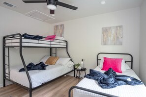A room with two bunk beds, a ceiling fan, a small table with a lamp, and a painting on the wall. - Historic Comfort 2BR 1BA Guesthouse Near Riverwalk (San Antonio)