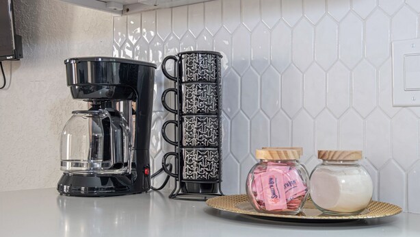 A kitchen counter with a coffee maker, a stack of patterned mugs, and two jars with lids. - Historic Comfort 2BR 1BA Guesthouse Near Riverwalk (San Antonio)